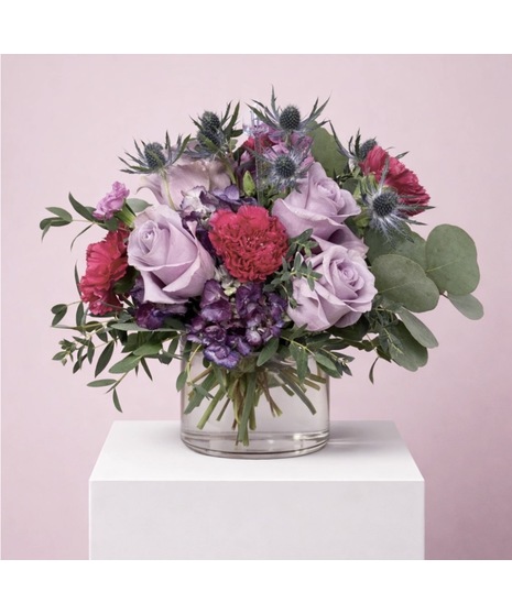 magenta flowers with green filler around them in a low glass container